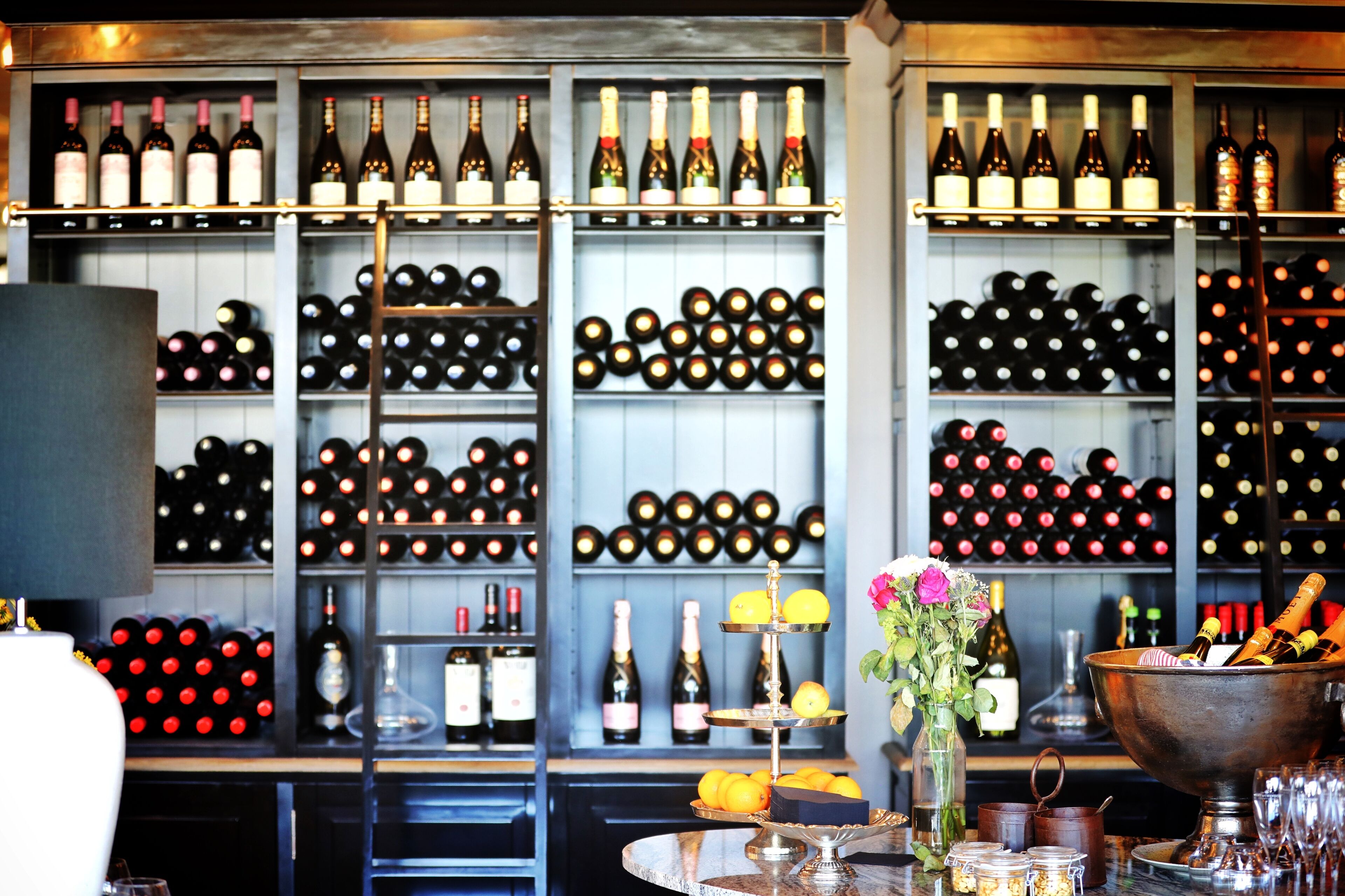 Una zona de bar con estantes llenos de botellas de vino y una variedad de copas y botellas sobre la barra.