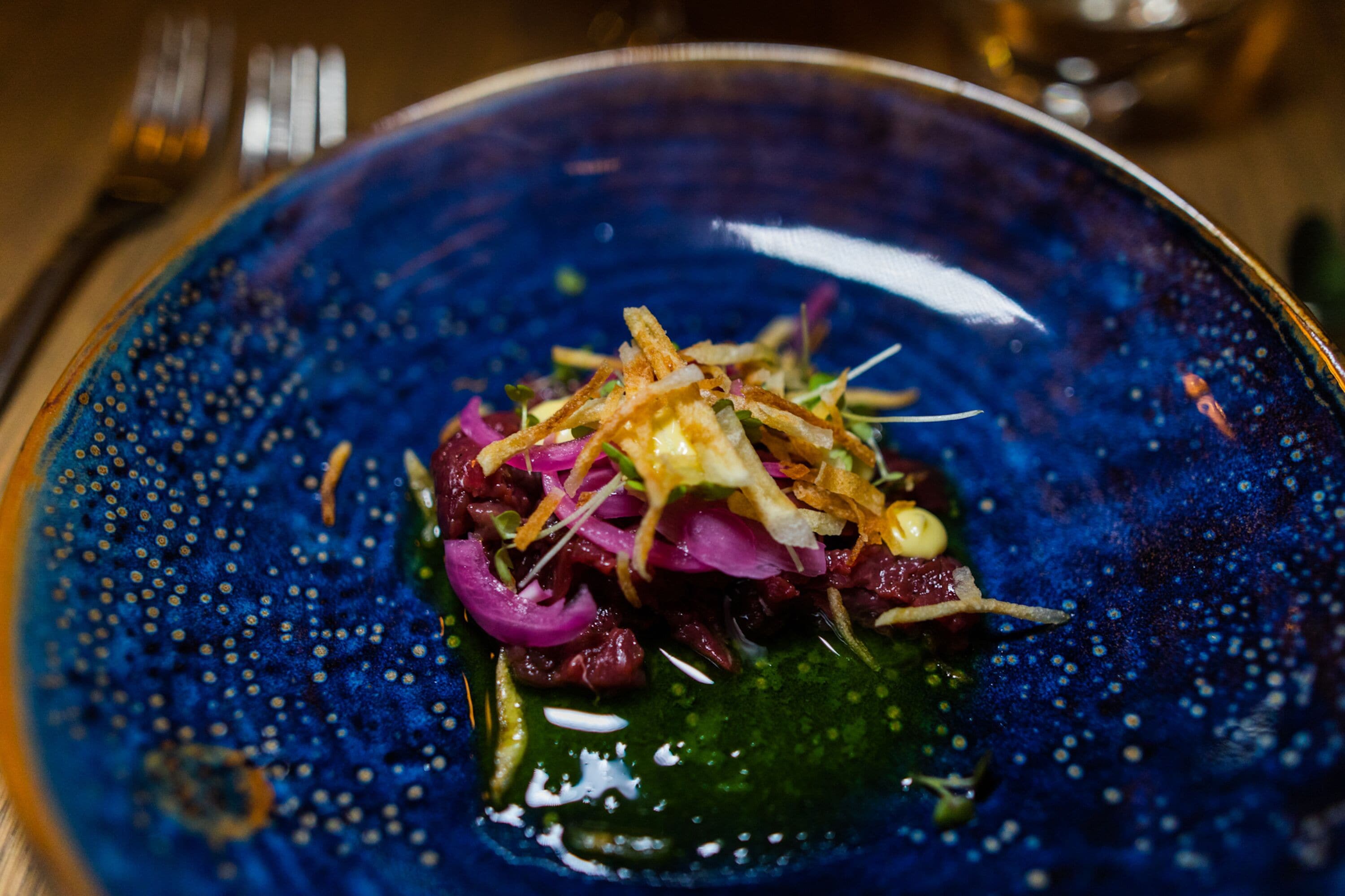 Une assiette bleue garnie d’une sauce verte, de chou rouge et de garnitures croustillantes.