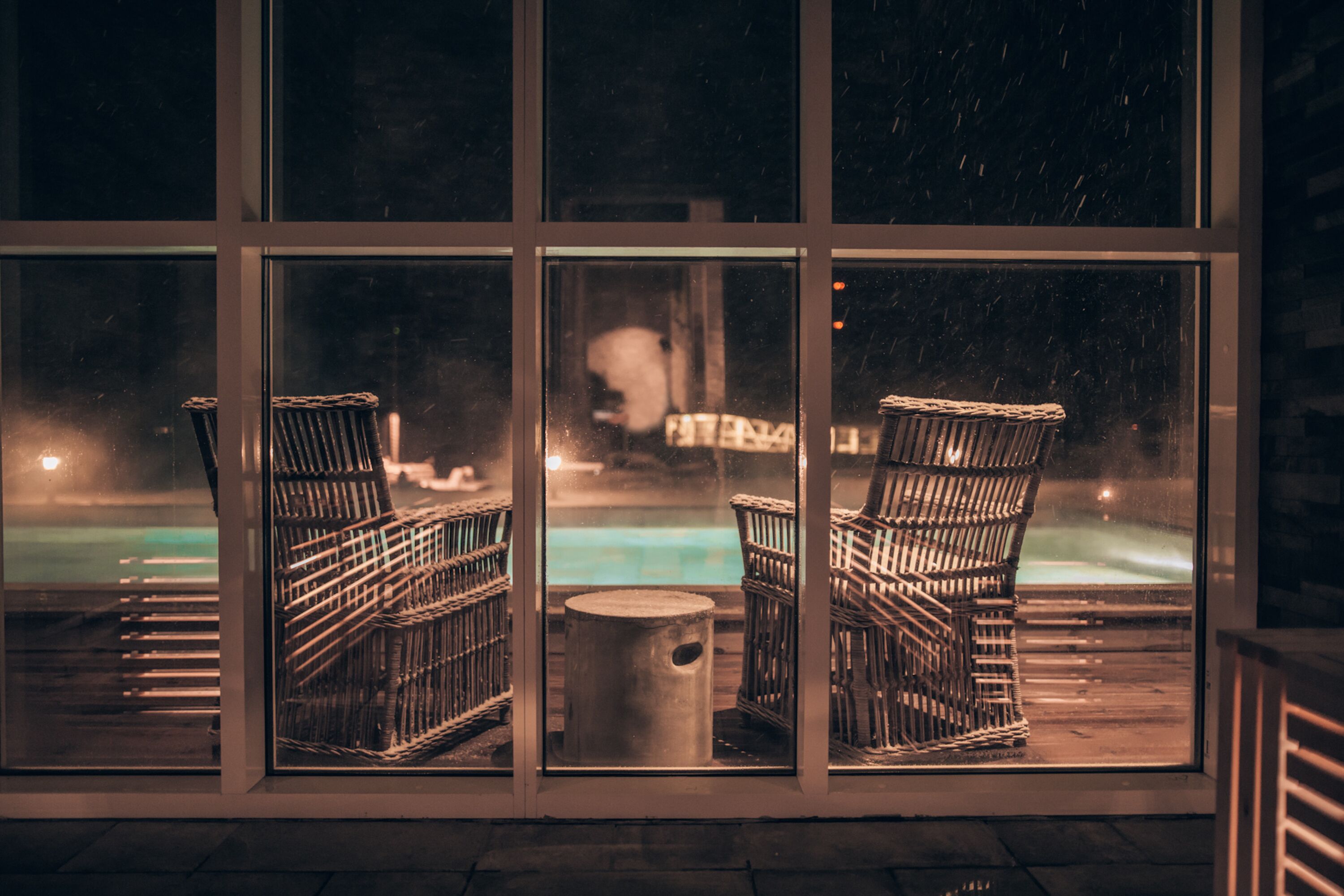 Duas cadeiras de vime voltadas para uma piscina, com um pedestal de pedra no meio.