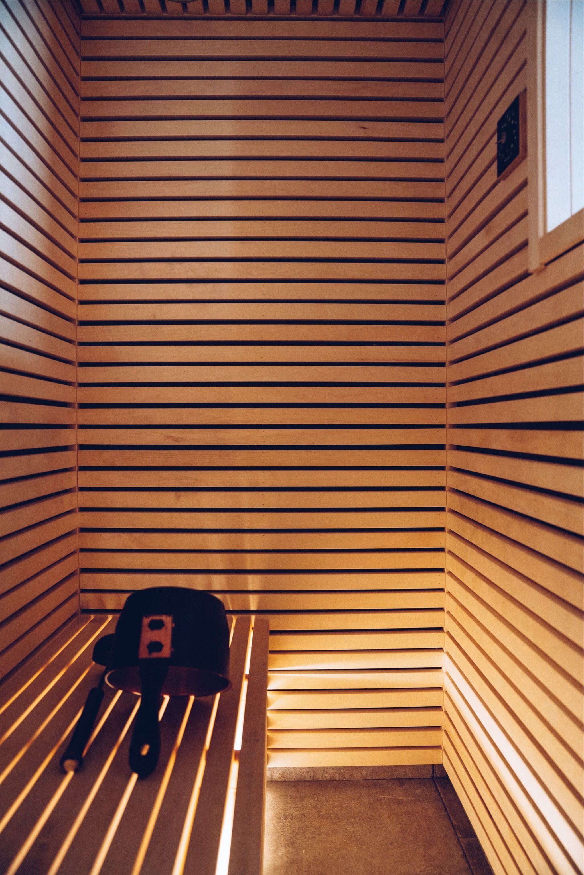 A sauna with wooden slats on the walls and a bench with a towel and a hat.
