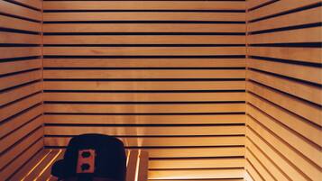 A sauna with wooden slats on the walls and a bench with a towel and a hat.