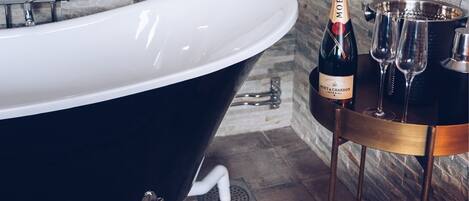 A modern bathroom with a freestanding bathtub, a wine bottle, and glasses on a metal stand.