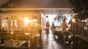 Ein Restaurant mit Holzboden, Tischen und Stühlen. Personen speisen, und es gibt eine Bar mit einer Theke.