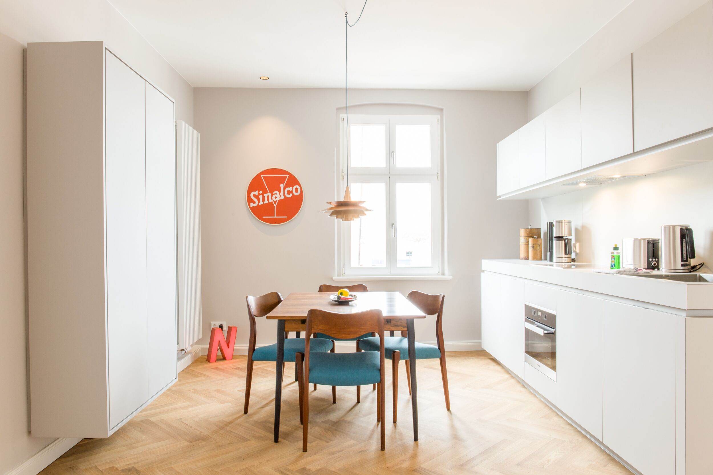 Una cocina moderna con armarios blancos, una mesa de comedor de madera con sillas azules y un ventanal con vistas al exterior.