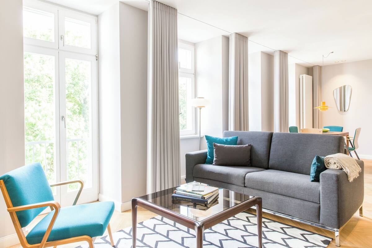 Un salon moderne avec un canapé gris, un fauteuil turquoise et une table basse en verre.