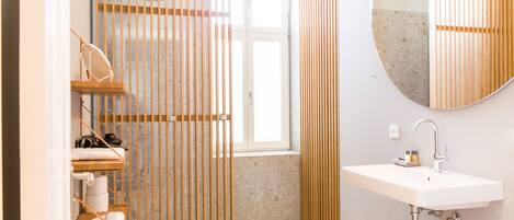 A modern bathroom with a wooden partition, a round mirror, a white sink, and a small stool.