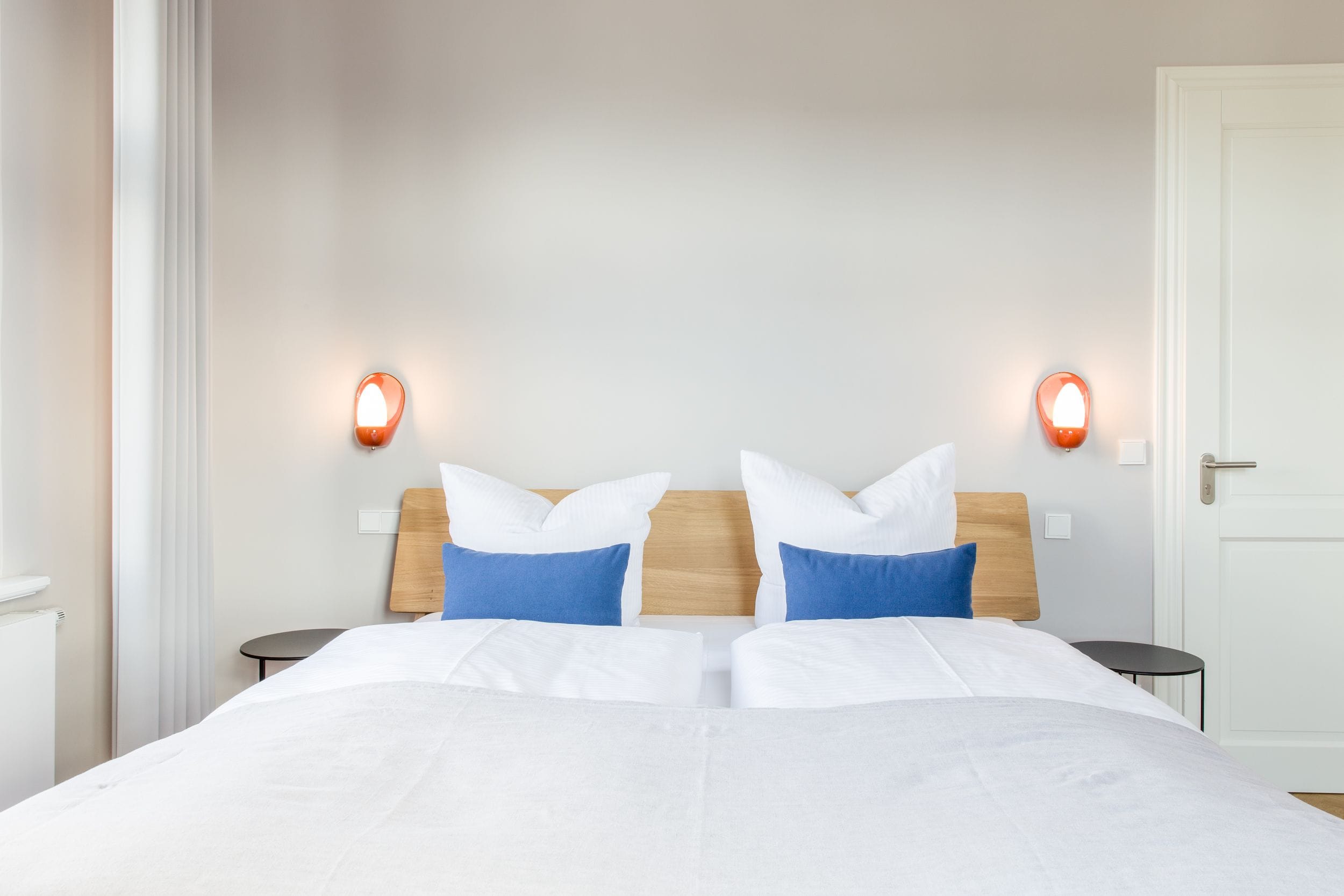 Een tweepersoonsbed met wit- en blauwe beddengoed, twee nachtkastjes en wandlampen.