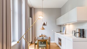 A modern kitchen with white cabinetry, a dining table with chairs, a pendant light, and a window with curtains. - OSTKÜSTE - Nadler Hof Design Apartments (Heringsdorf)