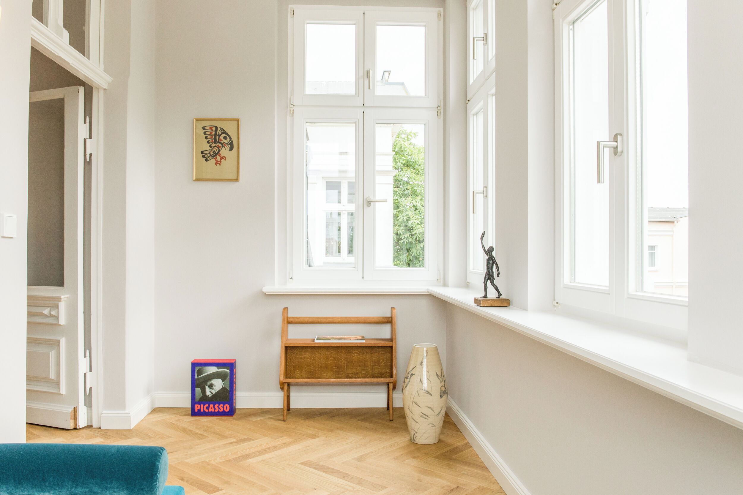 A room with a wooden bench, a vase, and a Picasso book on the floor.