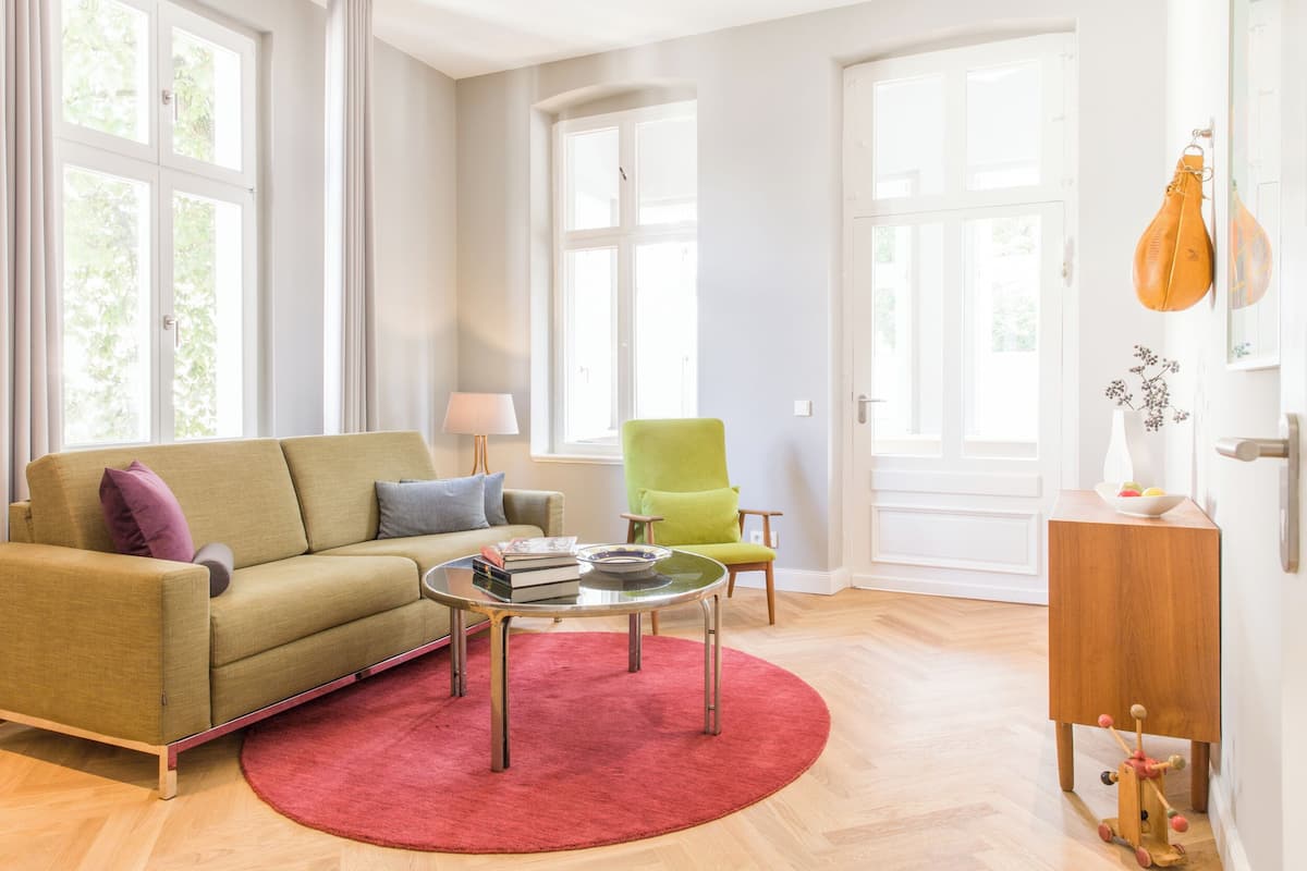 Un salon avec un canapé vert, un tapis rouge, une table d’appoint en bois et un fauteuil vert.