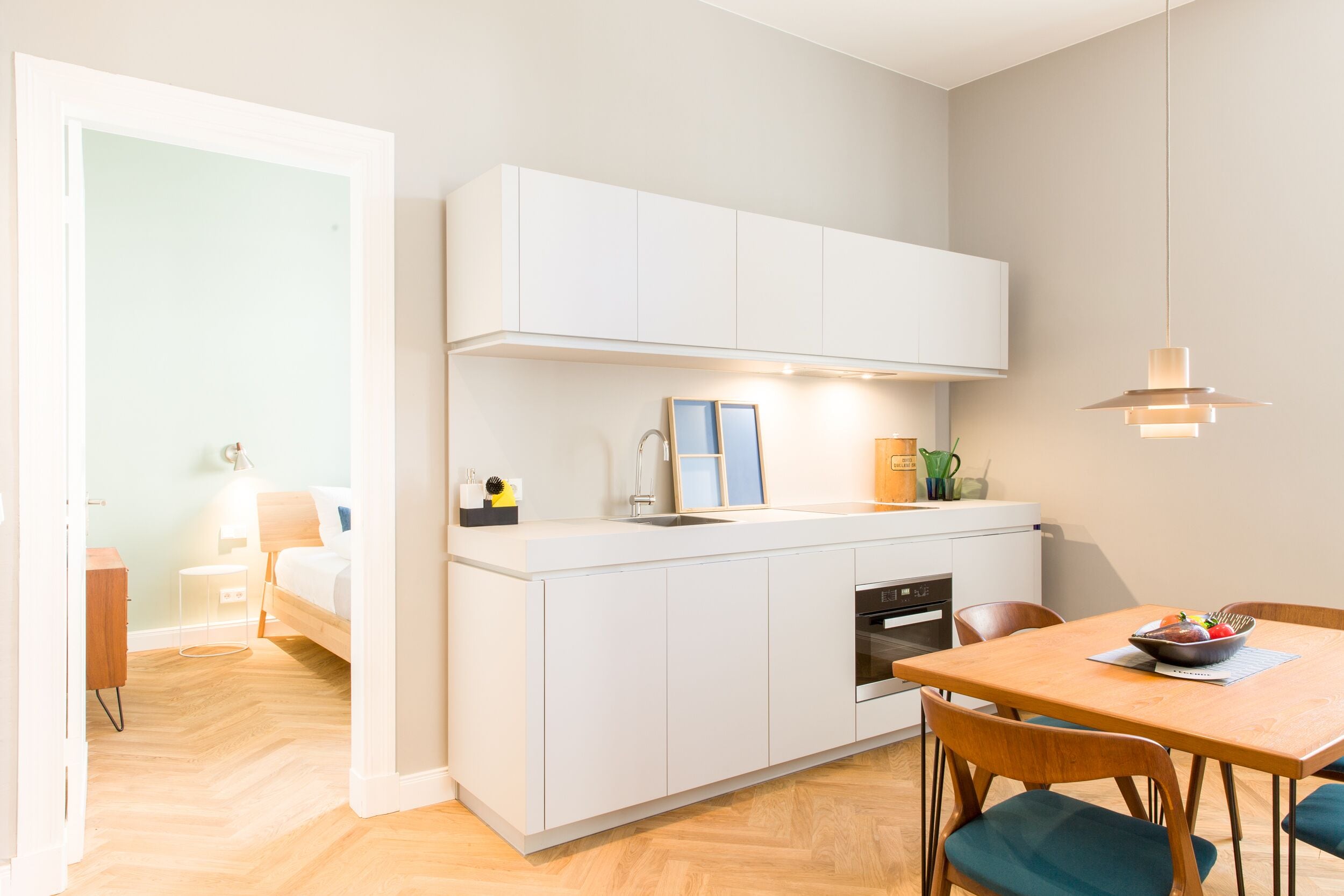 A compact kitchen with white cabinets, a built-in oven, and a dining area with a wooden table and chairs.