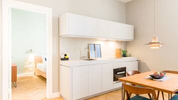 A compact kitchen with white cabinets, a built-in oven, and a dining area with a wooden table and chairs.