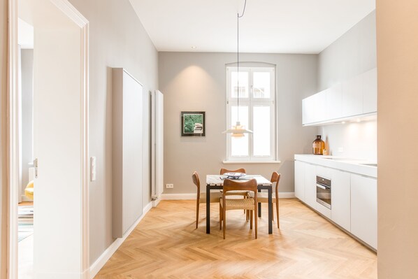 Une cuisine moderne avec des meubles blancs, une table à manger avec des chaises, une fenêtre et un luminaire suspendu.