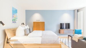 A modern bedroom with a wooden bed, a TV, a wardrobe, and a sofa. - OSTKÜSTE - Nadler Hof Design Apartments (Heringsdorf)