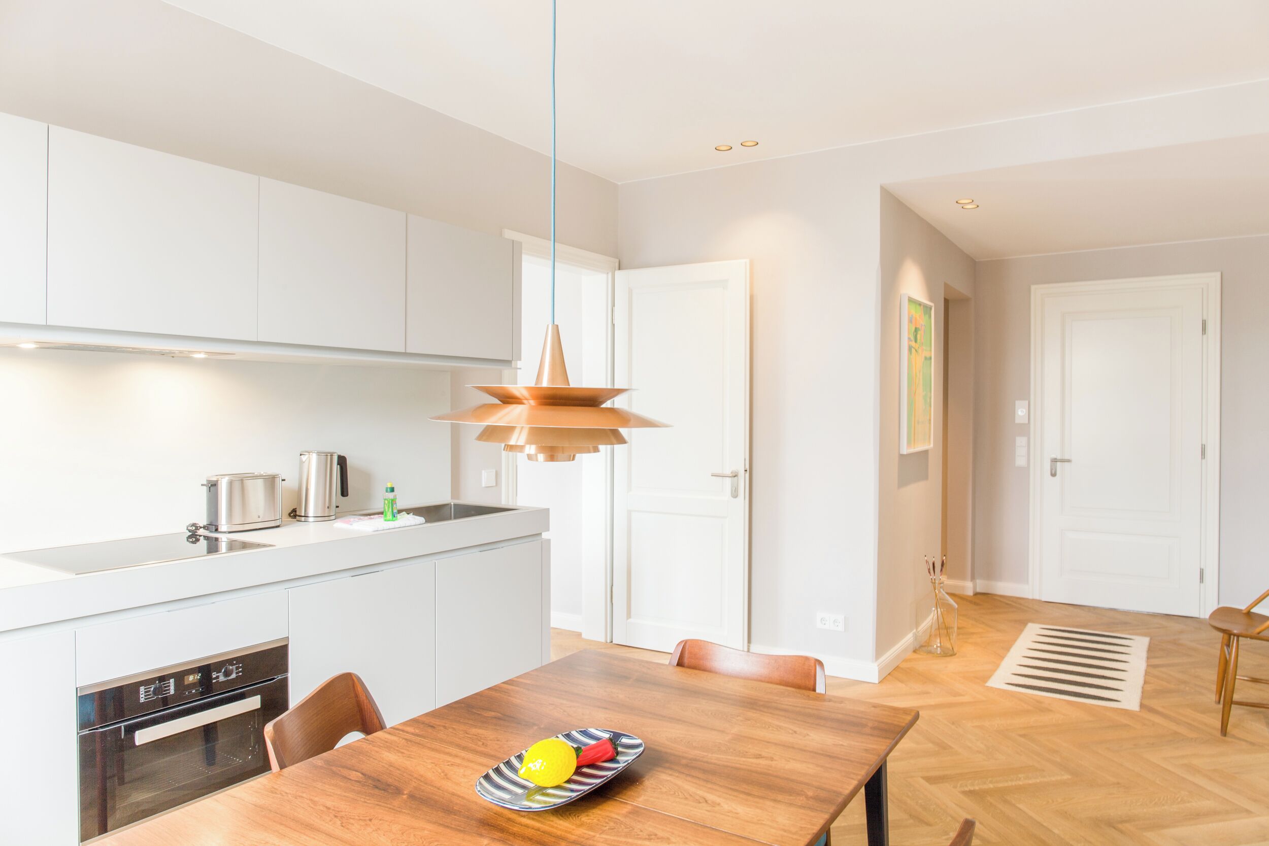 A modern kitchen with white cabinets, a wooden dining table, and a pendant light.