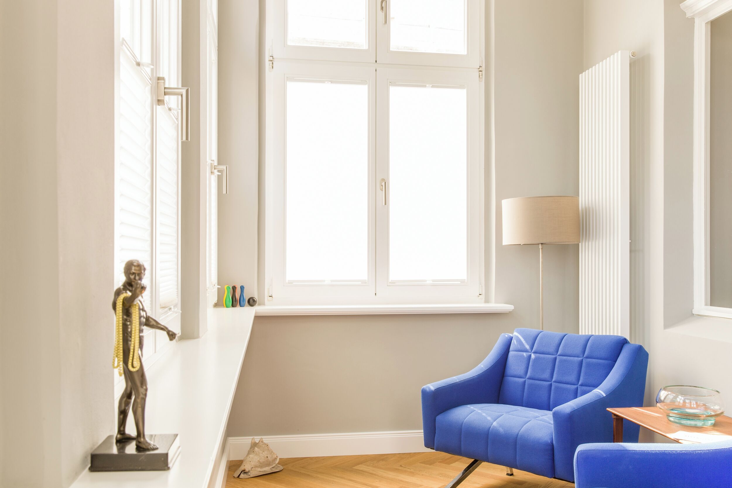 A room with a blue armchair, a statue, a radiator, and a window with blinds.