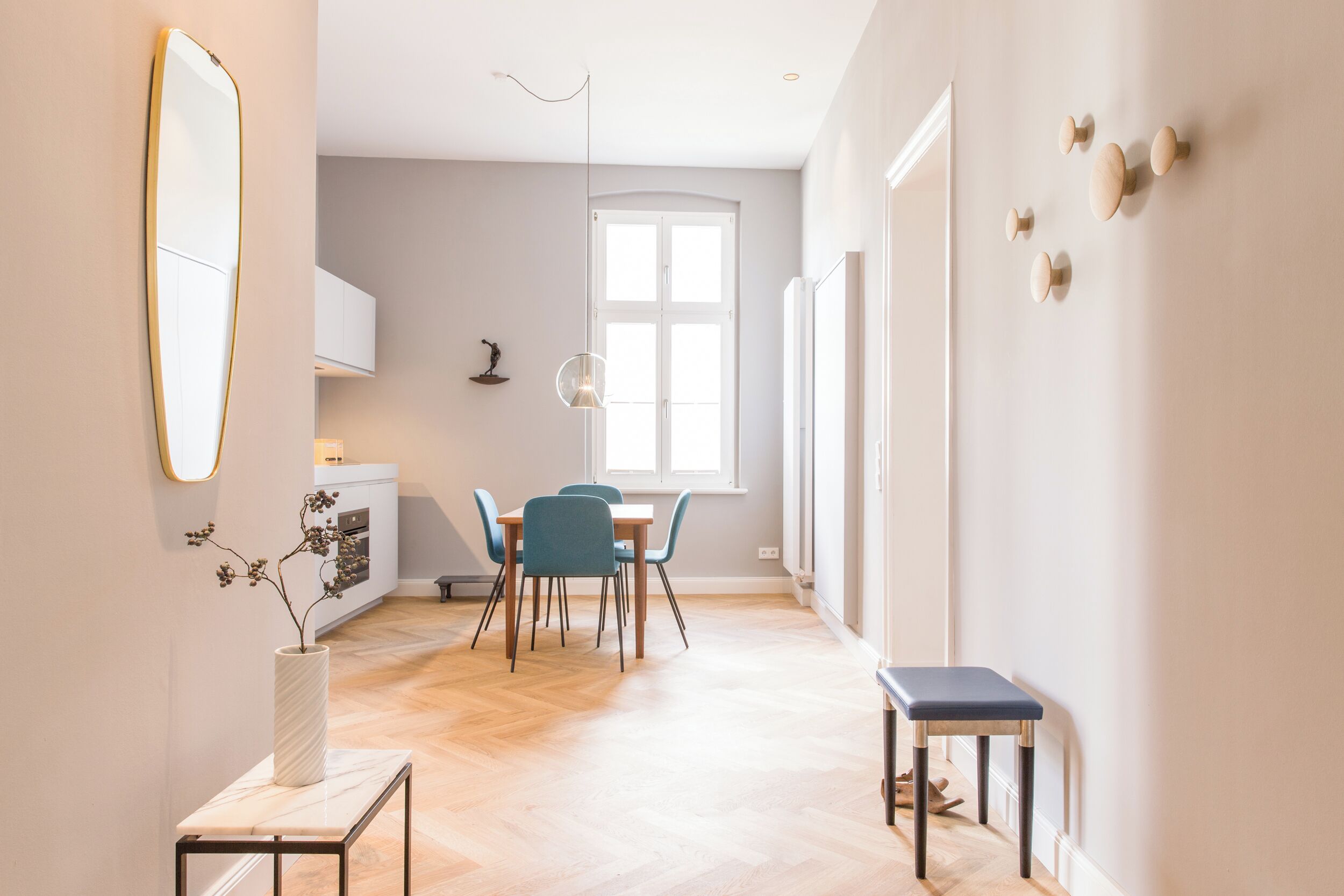 A modern, well-lit dining area with a wooden floor, a white table, and blue chairs.