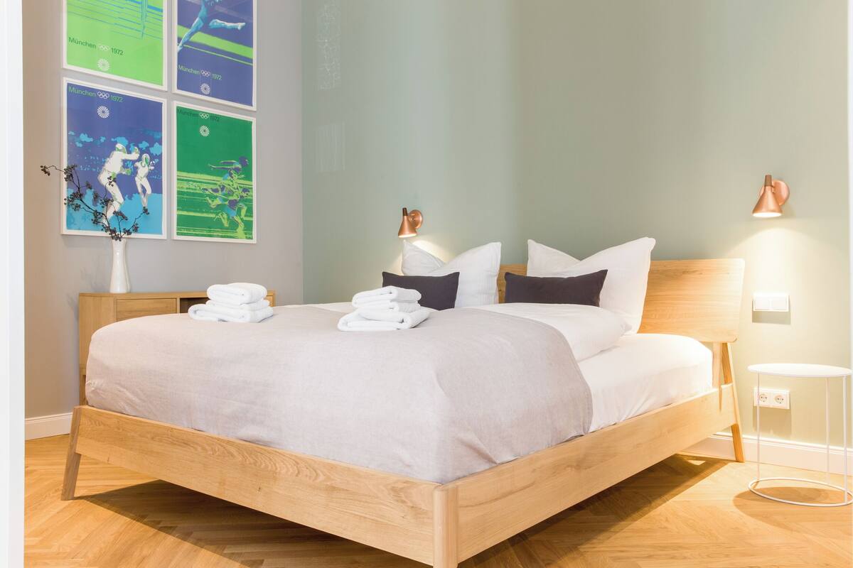 Un lit bien fait, avec du linge de lit et des serviettes blanches, une tête de lit en bois et une table de chevet avec une lampe.