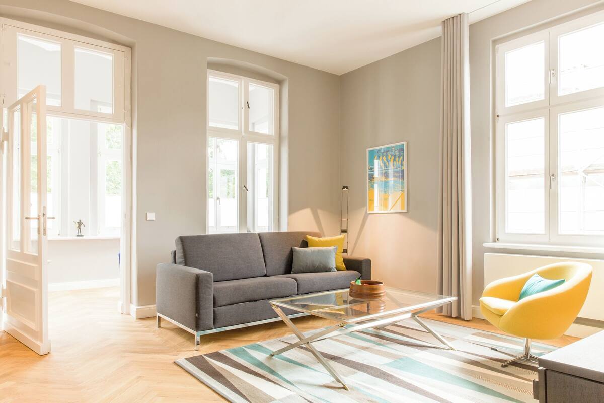 Un salon moderne avec un canapé gris, un fauteuil jaune et une table basse en verre.
