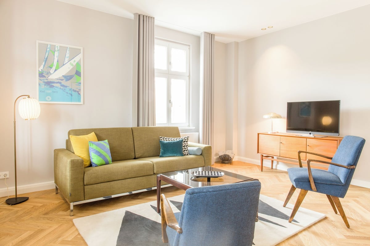 Un salon moderne avec un canapé, un fauteuil et un téléviseur à écran plat posé sur un meuble en bois.