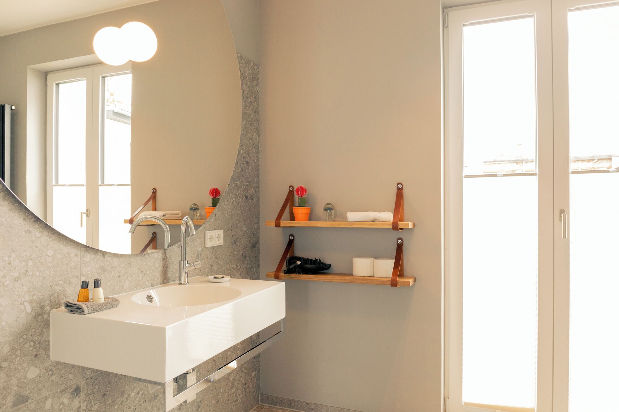 A bathroom with a white sink, a mirror, and wooden shelves with toiletries.