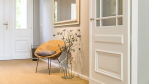 A room with a wicker chair, a glass vase with flowers, and a white door with a mirror above it. - OSTKÜSTE - Nadler Hof Design Apartments (Heringsdorf)