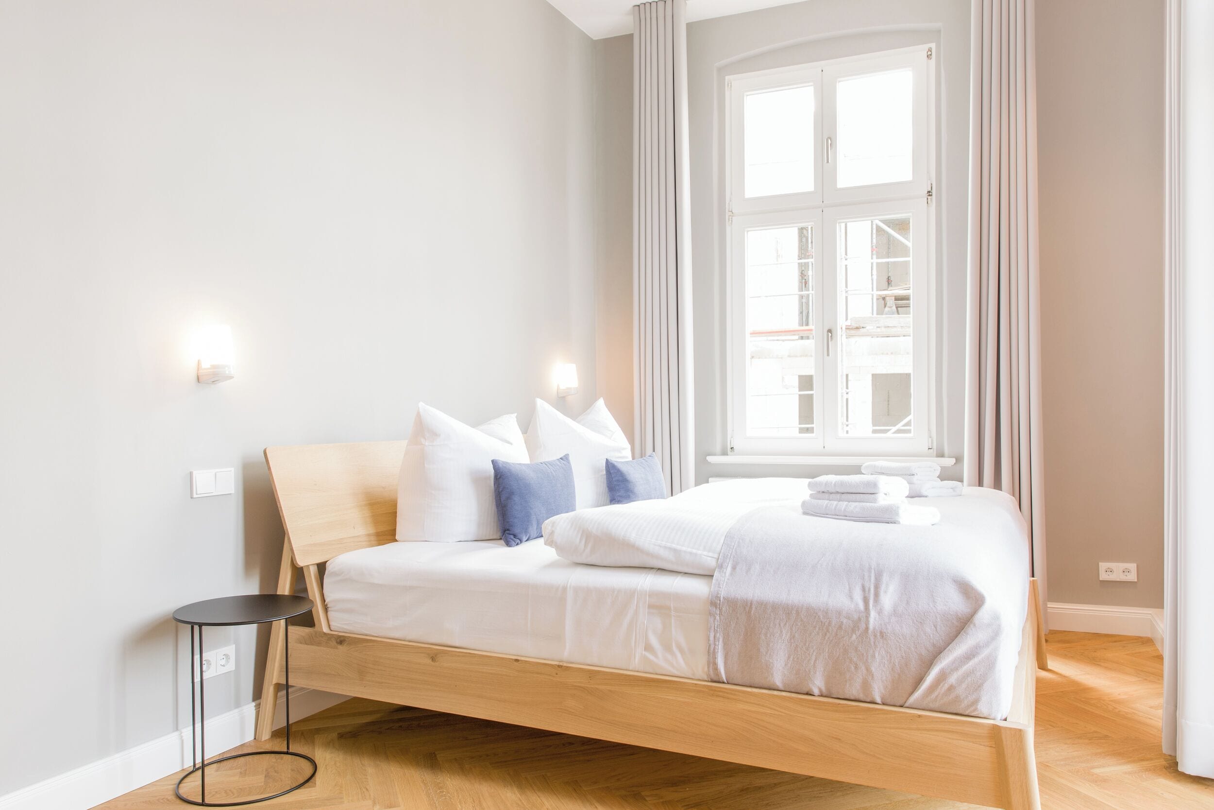 A modern bedroom with a wooden bed, white bedding, and a small bedside table.