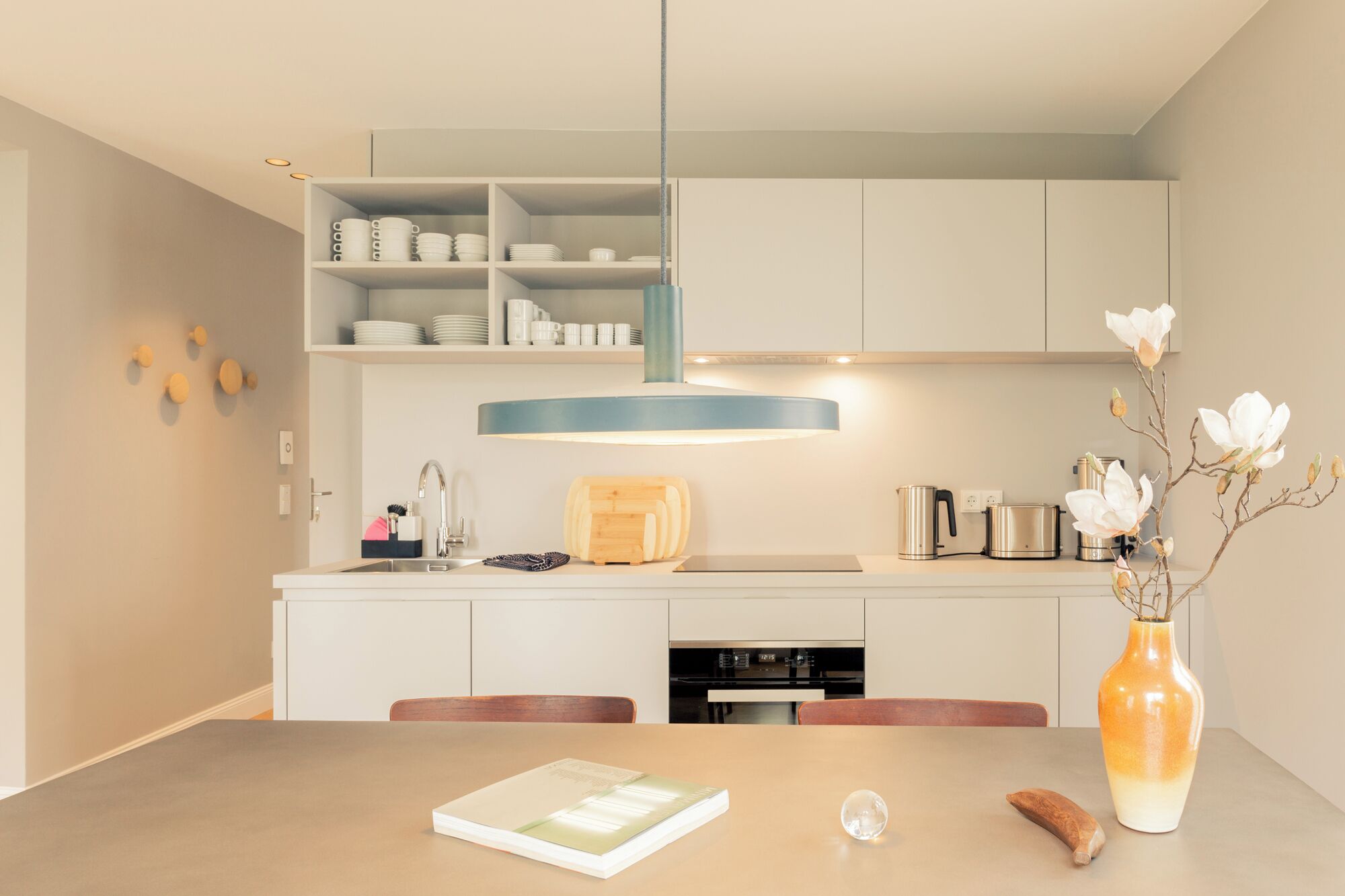 Una cocina moderna con gabinetes blancos, una isla central y una mesa de comedor con un libro y una banana.