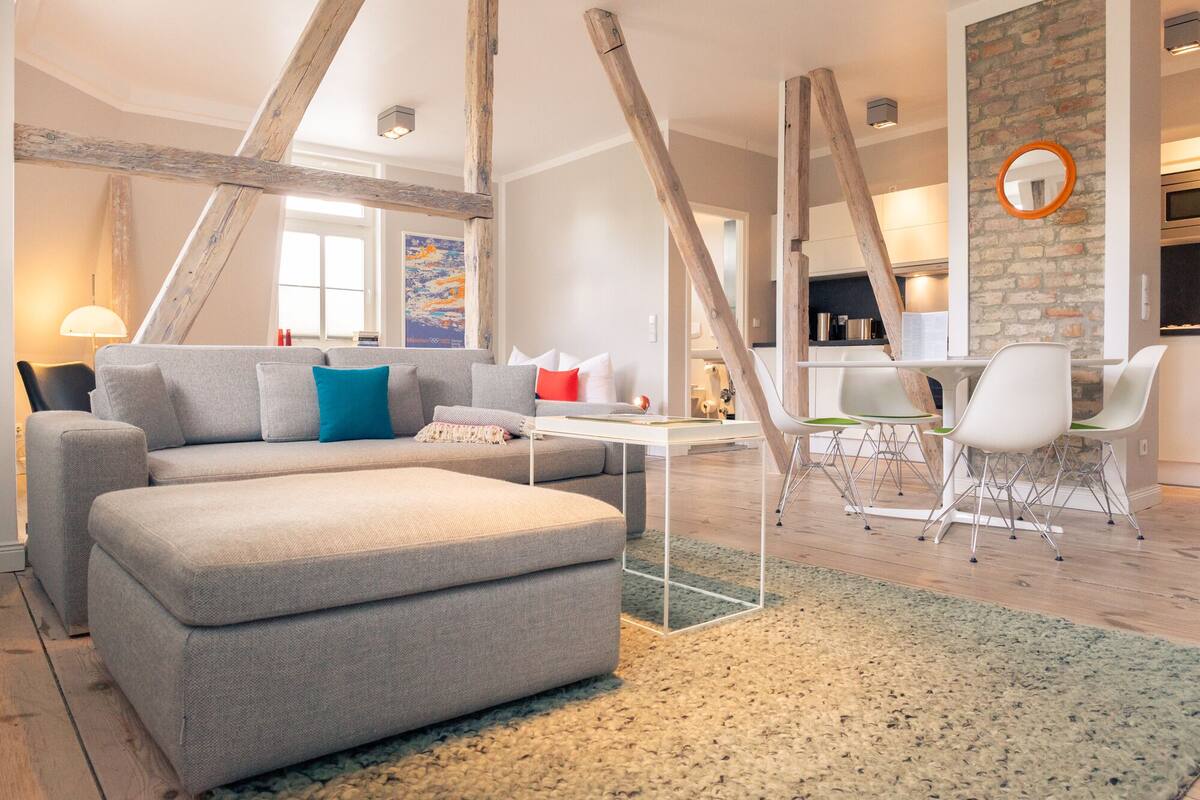 Een moderne woonkamer met een grijze bank, een salontafel en een eethoek met witte stoelen.