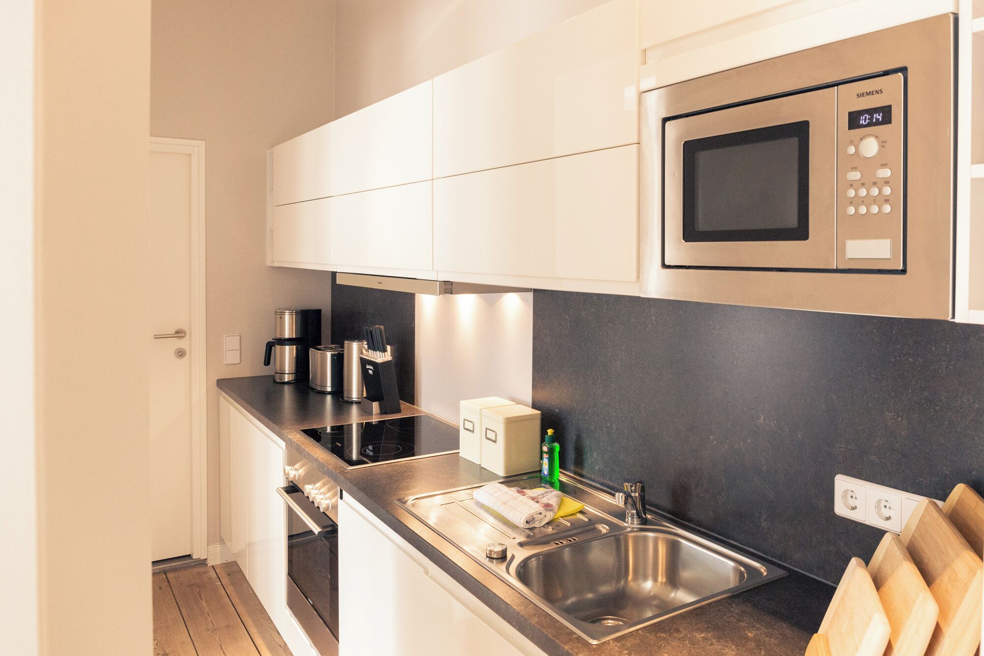 A modern kitchen with white cabinets, a stainless steel sink, a microwave, and a coffee maker.