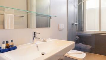 Une salle de bain moderne avec un grand lavabo blanc, une étagère en verre au-dessus et une douche séparée par des parois en verre.