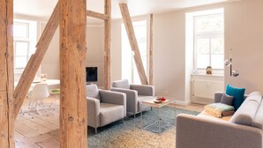 A modern living room with exposed wooden beams, a grey sofa, a small table with a bowl, and a TV in the background. - OSTKÜSTE - Villa Albatros Design Apartments (Heringsdorf)