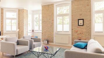 A modern living room with a brick wall, large windows, and a glass coffee table.
