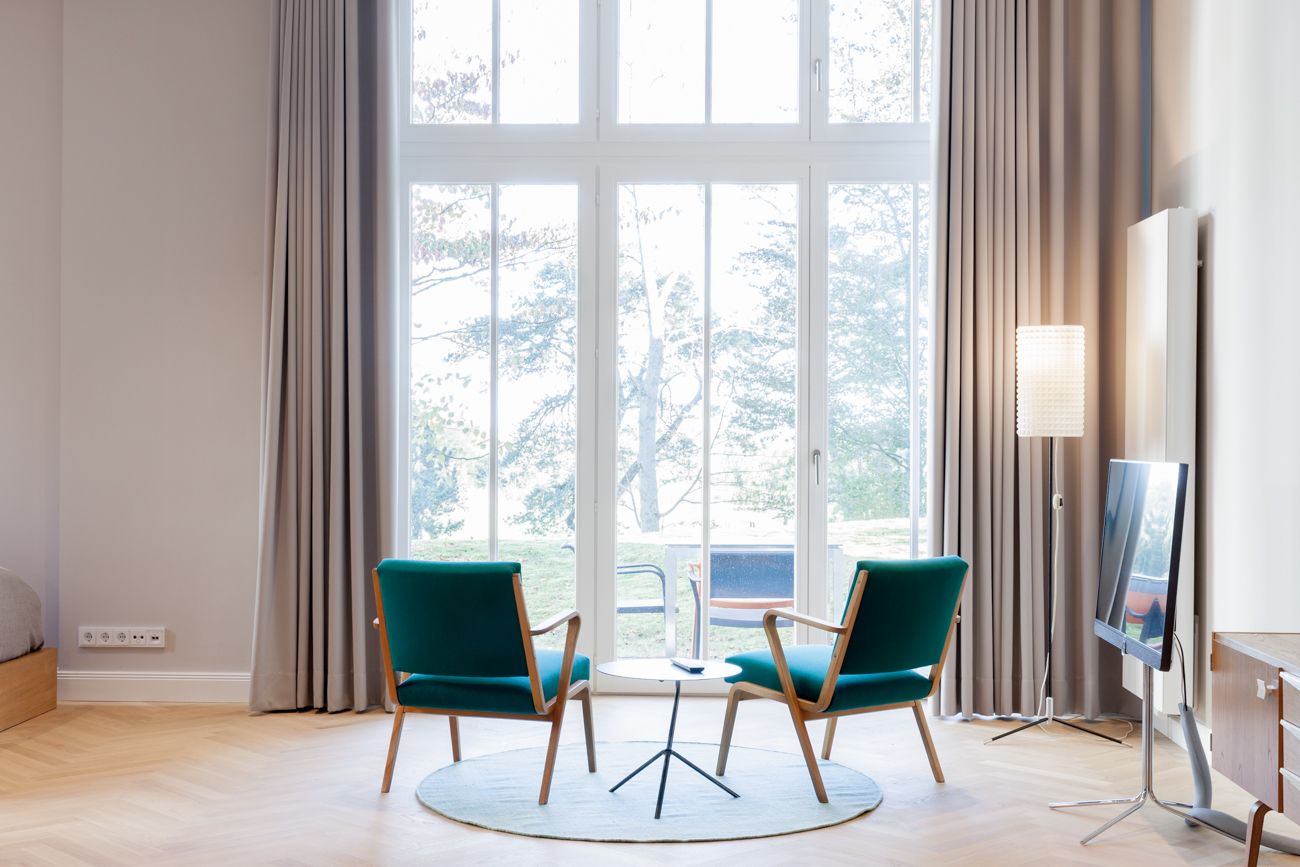 Une pièce moderne avec deux fauteuils turquoise, une petite table ronde et un téléviseur posé sur un meuble.