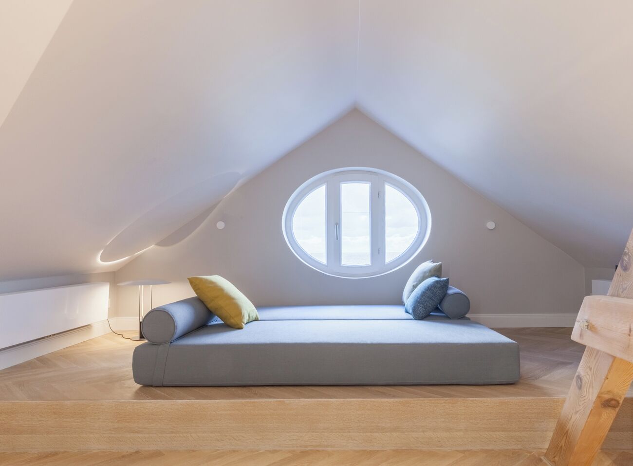 Dormitorio tipo loft con tragaluz, sofá cama y suelo de madera.