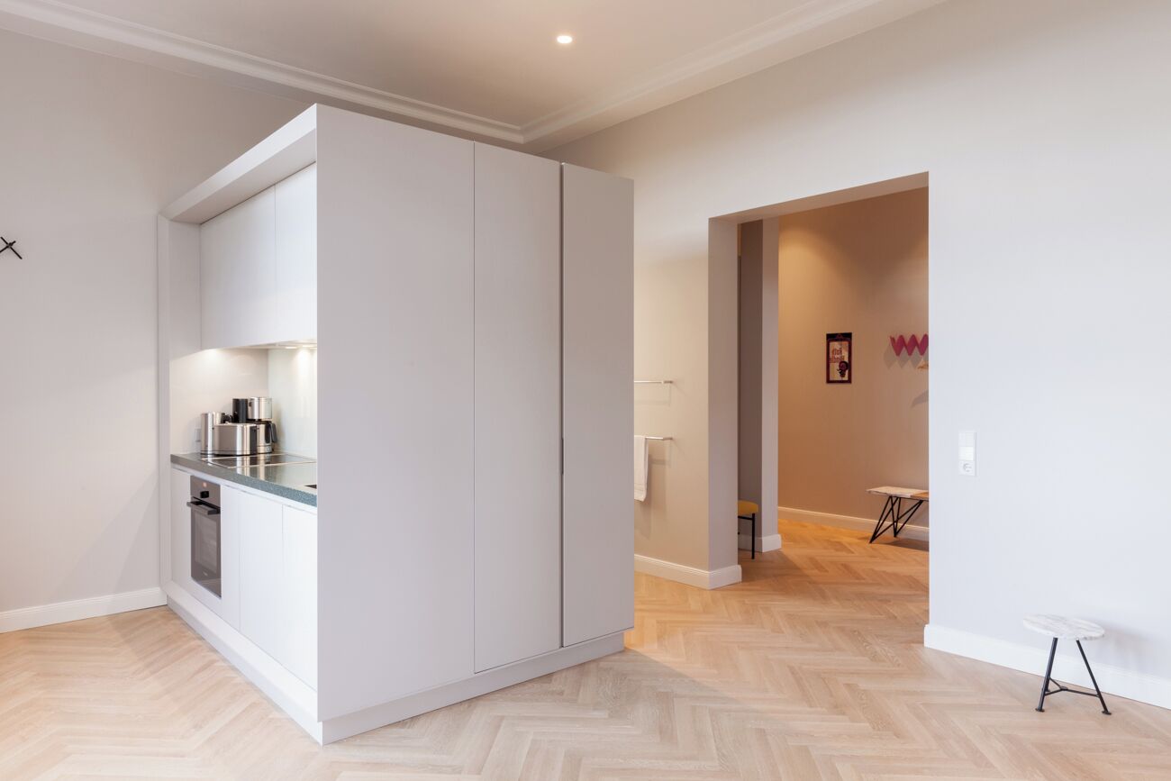 A modern kitchen with white cabinets, a stainless steel countertop, and a built-in oven.