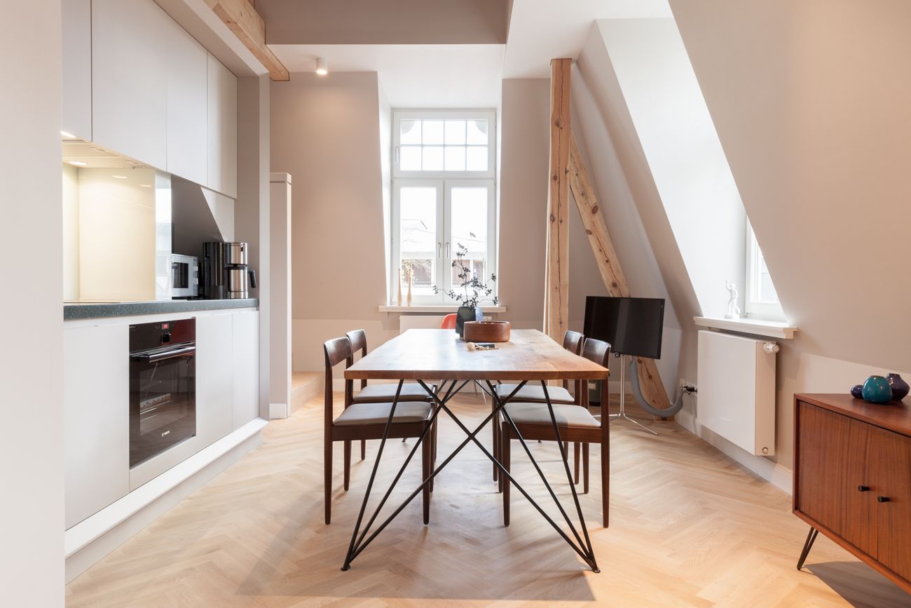 A modern kitchen with a dining area, featuring a large window, wooden flooring, and a loft-style ceiling.