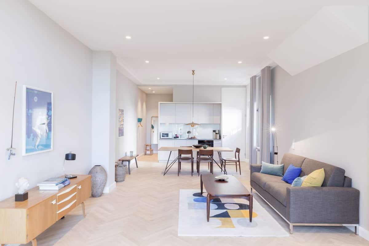 A modern living room with a sofa, coffee table, and a dining area with chairs and a table.