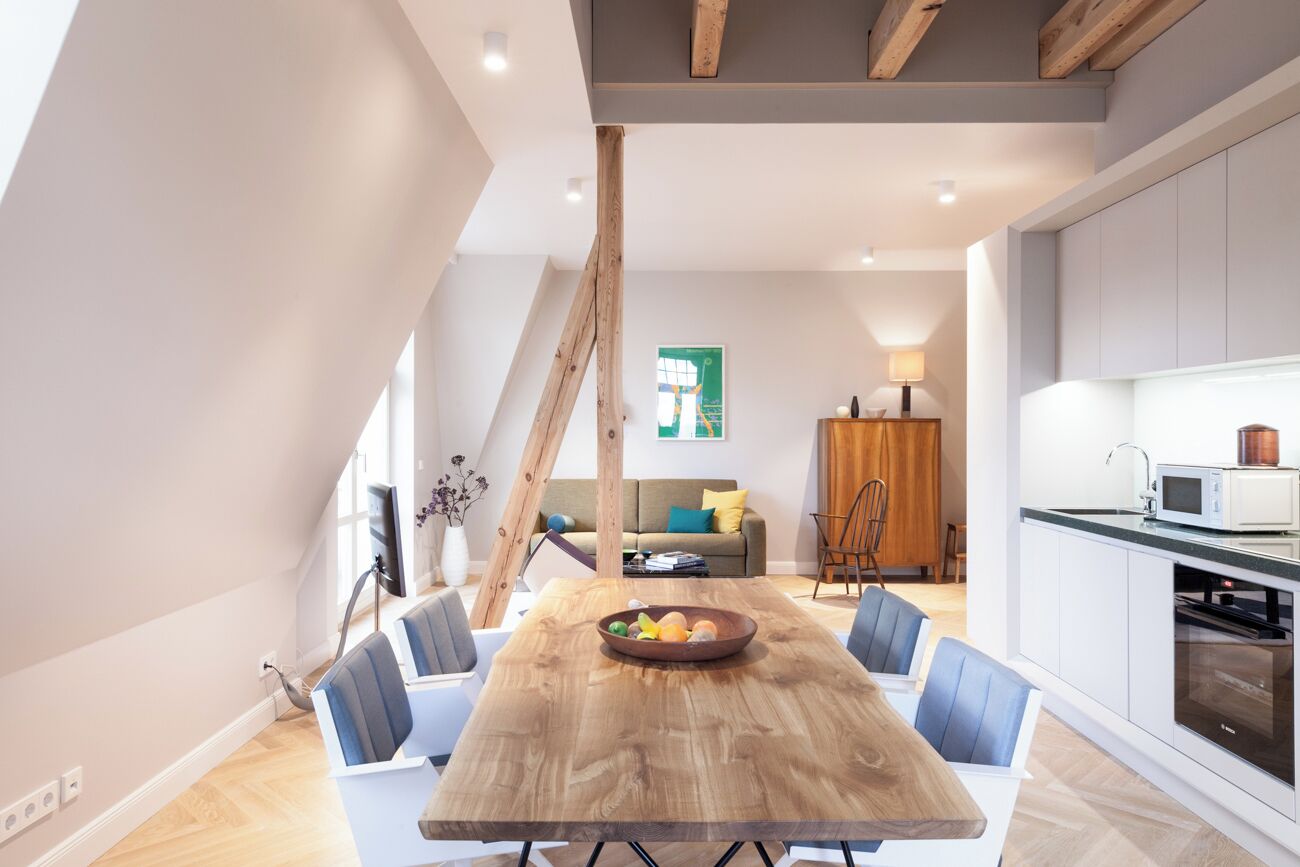 A modern kitchen with white cabinets, a wooden dining table, and a fruit bowl.