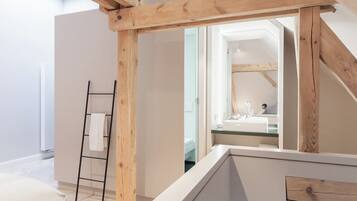 Un baño moderno con estructura de techo de madera, cabina de ducha de vidrio y zona de lavamanos visible.