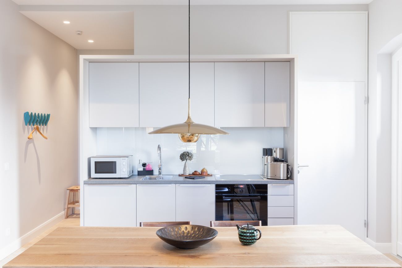 A modern kitchen with white cabinets, a wooden dining table, and a hanging pendant light.