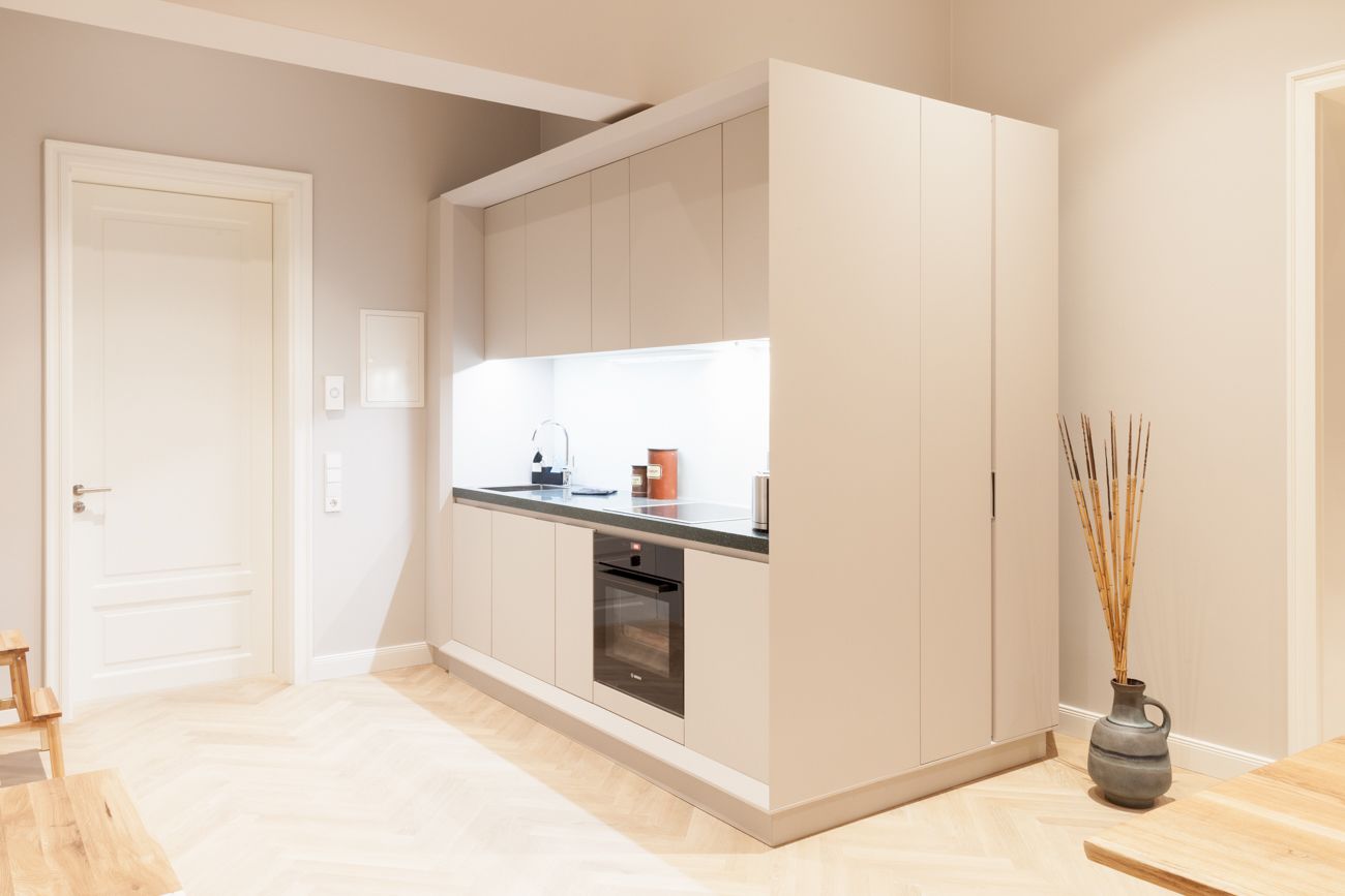 A modern kitchen with built-in appliances, a wooden floor, and a vase with reeds.