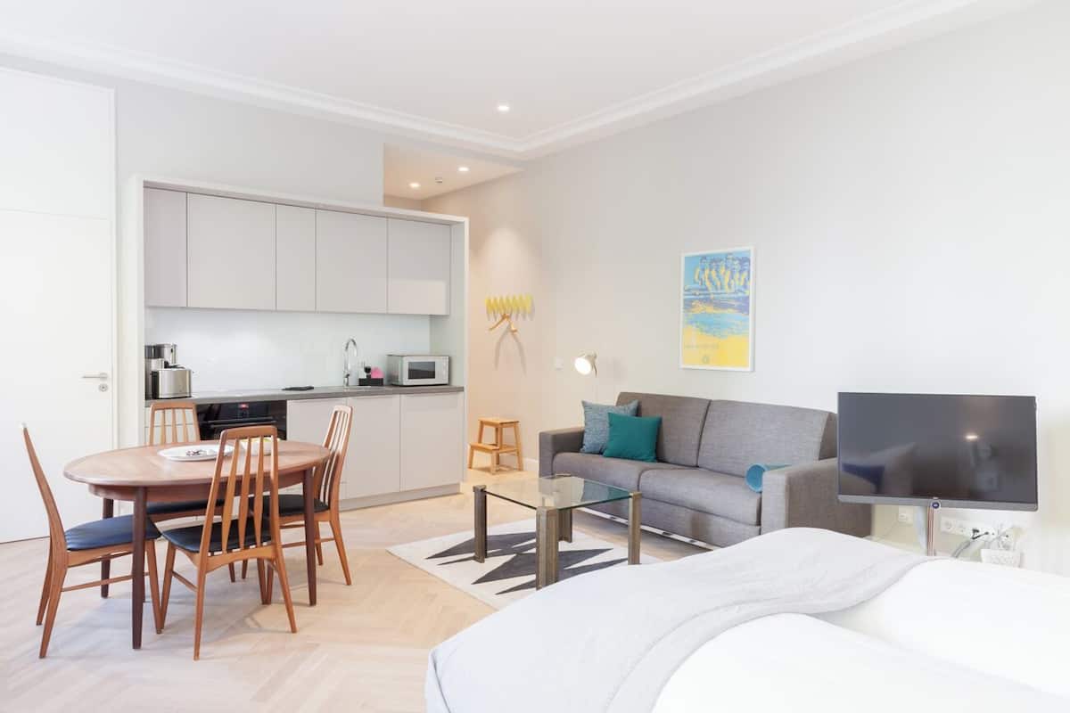 A modern living room with a sofa, a TV, and a dining area with a table and chairs.
