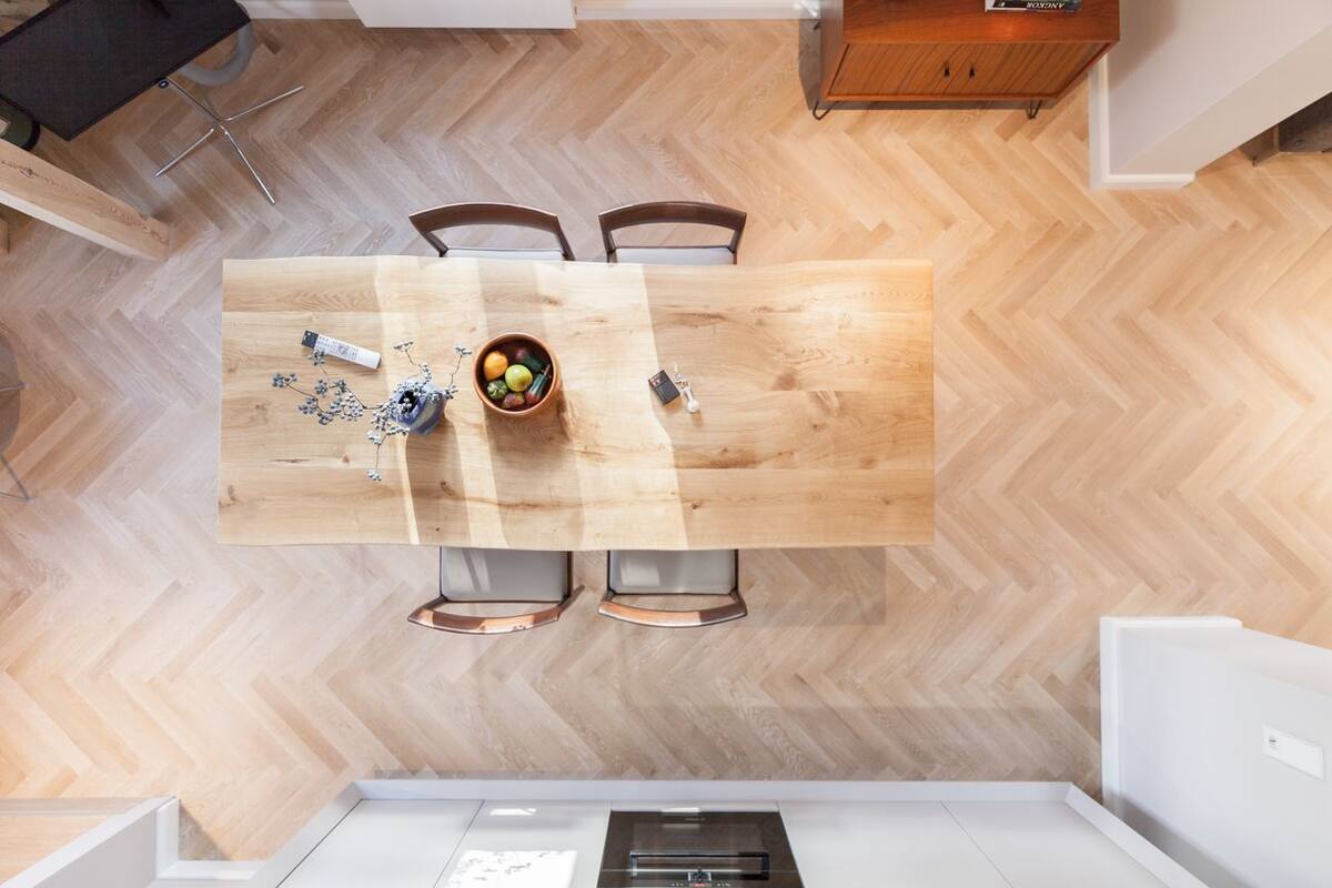 A modern kitchen with a wooden herringbone floor, a central island with chairs, and a built-in oven.