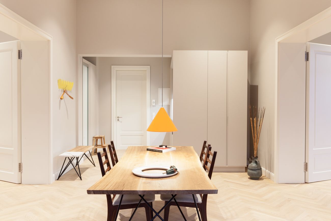 Een eethoek met een houten tafel, stoelen, een hanglamp en een deur op de achtergrond.