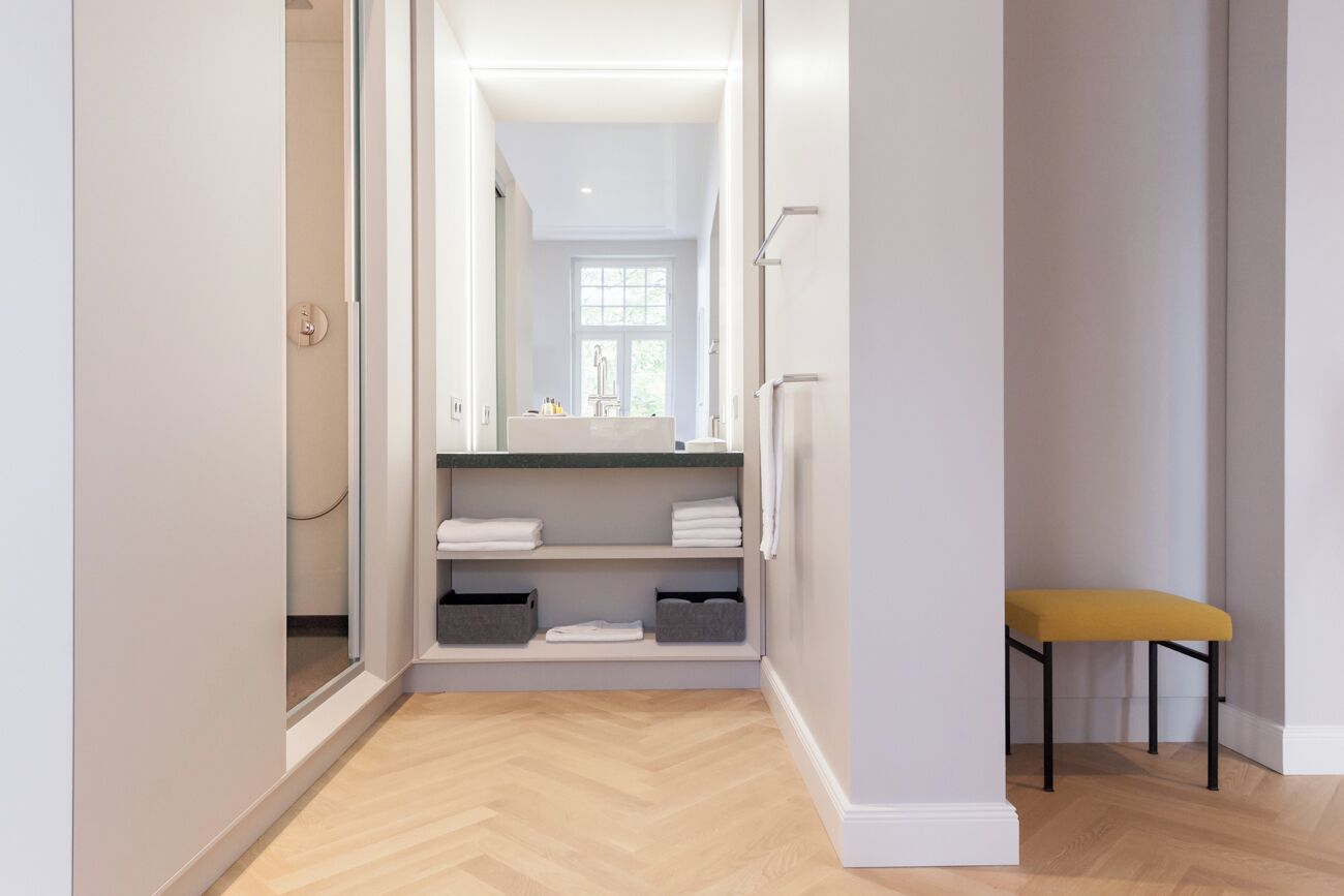 Un pasillo con suelo de madera, un banco y una puerta de cristal que da al baño.