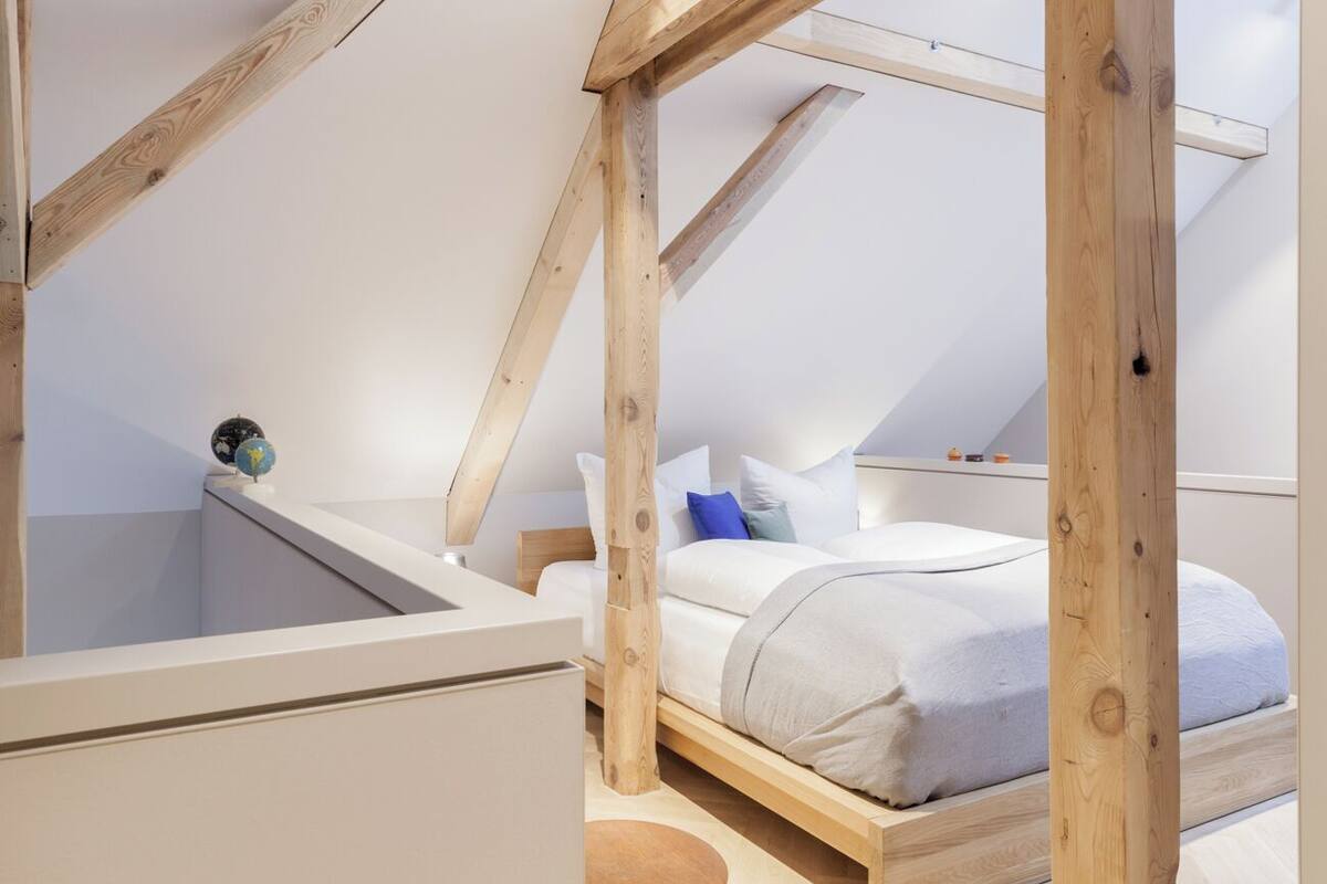 A bedroom with a sloped ceiling, wooden beams, a bed with white bedding, and a small globe on the nightstand.