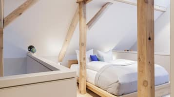 Une chambre avec un plafond en pente, des poutres en bois, un lit avec une literie blanche et un petit globe posé sur la table de chevet.