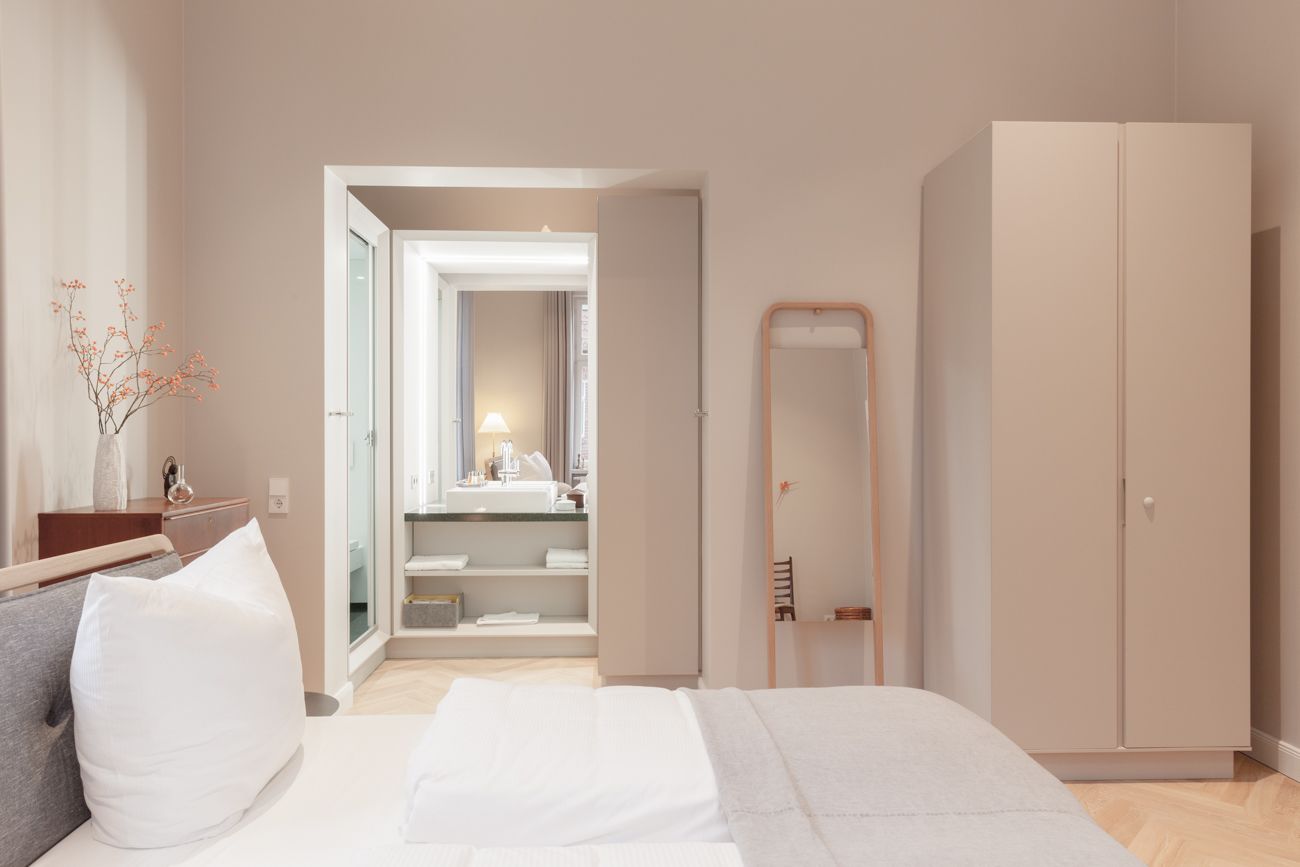 Een moderne slaapkamer met een bed, een kledingkast, een spiegel en een zichtbare badkamer door een geopende deur.