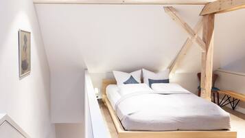 Un dormitorio con estructura de cama de madera, ropa de cama blanca y techo inclinado con vigas a la vista.